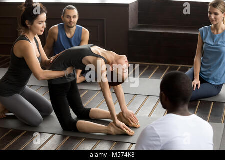 Teacher assisting woman l'apprentissage de nouvelles yoga pose à la formation de groupe Banque D'Images