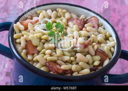 Vintage bleu pot de flageolets cuits au four avec des côtes de porc fumé sur une vieille planche de bois rose Banque D'Images