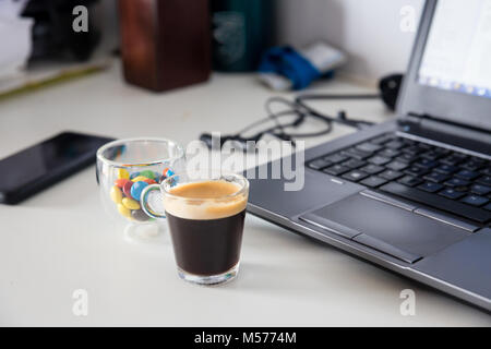 Tasse de café et une tasse de chocolat colorés remplis de bonbons à côté d'un ordinateur portable, le snack idéal combinaison pour travailler Banque D'Images