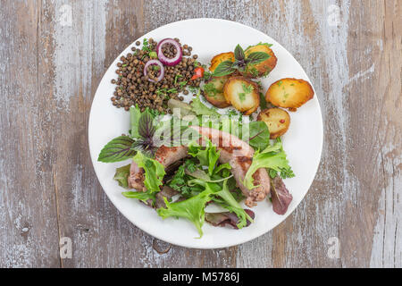 France La saucisse de Toulouse grillée avec potatoaes rôti et salade et lentilles sur le vieux fond de bois Banque D'Images