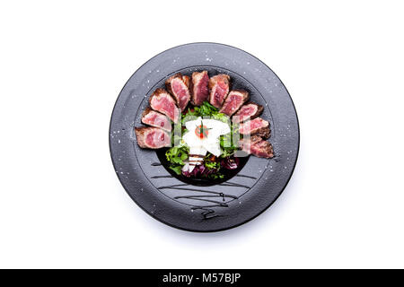 Biftecks juteux steak de boeuf saignante avec épices coupées en tranches sur la plaque en ardoise avec de l'ail frit et salade d'épinards. style sombre, vue de dessus, à proximité- Banque D'Images