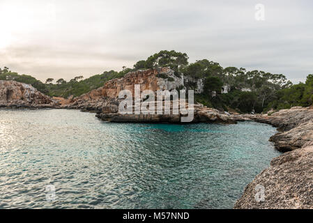 Le coucher du soleil et une formation rocheuse dans l'eau de la mer méditerranée vu depuis le Caló des Moro sur l'île de Majorque, Espagne. Banque D'Images