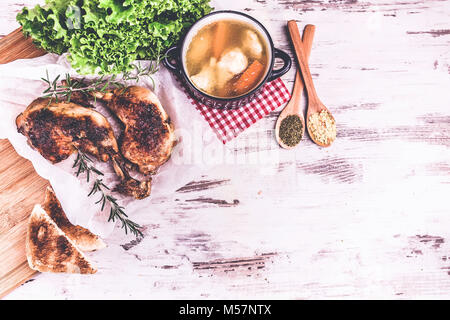 Délicieux pilons de poulet rôti au romarin et d'épices dans des cuillères et de la soupe au poulet servi dans un bol traditionnel sur un fond de bois rustique. Voir Banque D'Images