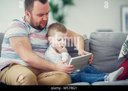 Photo de père à fils avec tablet assis sur un canapé gris Banque D'Images