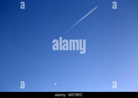 Avion avec trainées dans un fond bleu du ciel avec la lune Banque D'Images