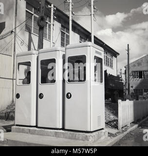 Journée à Tokyo, Japon, milieu des années 50, un tableau historique montrant une rangée de trois cabines publiques nouvellement installé, avec des personnes à l'intérieur des cabines étroites l'article faire des appels téléphoniques. Banque D'Images