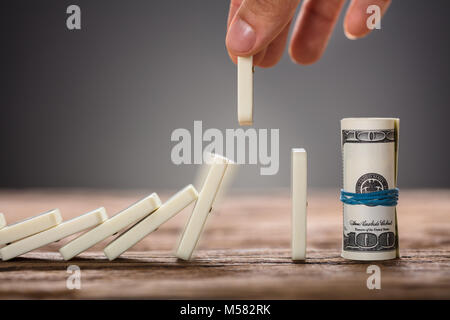 Portrait of businessman's hand picking pièce relevant domino vers roula des dollars sur la table Banque D'Images