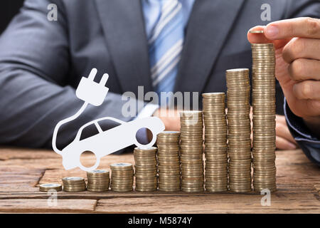 Portrait woman stacking coins avec la voiture électrique à table en bois Banque D'Images