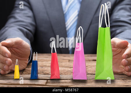 Portrait of businessman couvrant divers sacs shopping disposés en ordre croissant à table en bois Banque D'Images