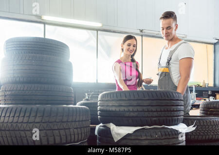 Belle auto mechanic aide une clientèle féminine de choisir entre différents pneus de haute qualité dans un atelier de réparation automobile contemporaine Banque D'Images