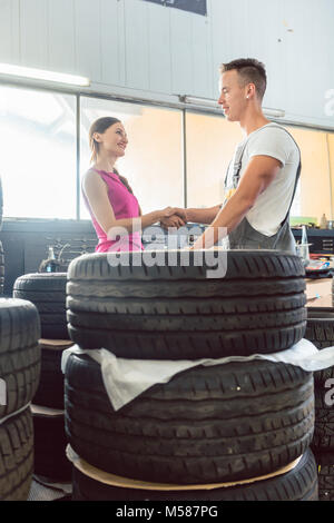 Belle auto mechanic aide une clientèle féminine de choisir entre différents pneus de haute qualité dans un atelier de réparation automobile contemporaine Banque D'Images