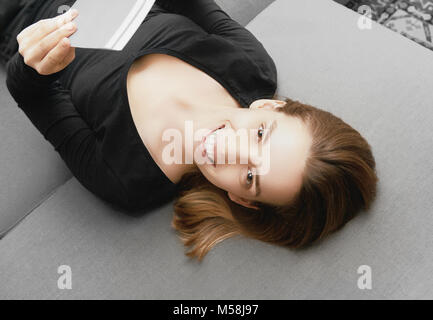 Woman smiling on sofà et la lecture d'un livre Banque D'Images