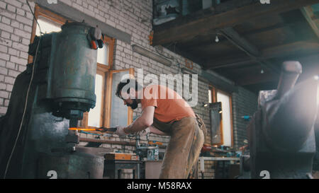 Homme forgeron forge le métal au marteau mécanique - petite entreprise Banque D'Images
