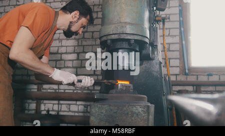 Homme forgeron forge le métal au marteau mécanique - petite entreprise Banque D'Images
