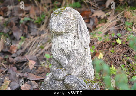 Close up of stone sculpture lapin altérés dans jardin avec arrière-plan de brindilles et fleurs sauvages feuilles marron re mémorial pour animal de lapin Banque D'Images