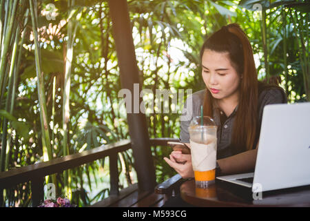 Belle femme utilisé Smartphone, ordinateur portable et thé glacé sur table des brown Banque D'Images