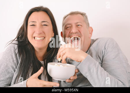 Amérique middle-aged couple laughing, eating popcorn et regarder un film ensemble. À l'intérieur Banque D'Images