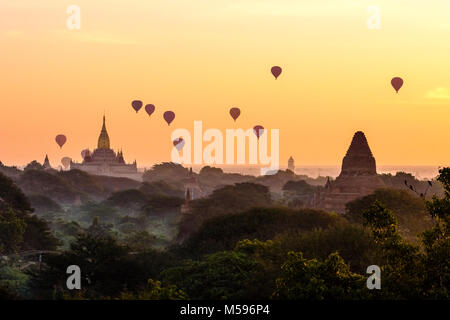 Les ballons à air chaud en survolant les pagodes de Bagan et les plaines brumeuses du site archéologique au lever du soleil Banque D'Images