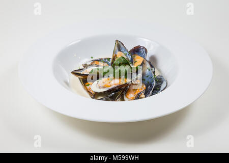 Moules dans une sauce crémeuse dans un bol blanc isolé sur fond blanc Banque D'Images