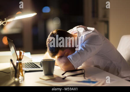 Homme d'affaires fatigué couché sur le tableau à l'office de nuit Banque D'Images