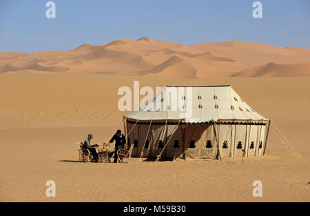 La Libye. Près de Ghat. VAN CASA mer de sable. Désert du Sahara. Les dunes de sable. Camp touristique dans la lecture et l'homme servir le thé à côté de la tente. Banque D'Images