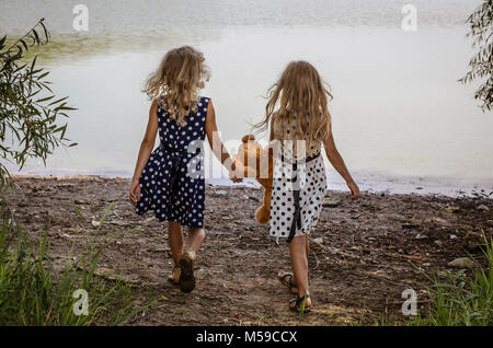 Deux petites filles avec de longs cheveux blonds holding a teddy bear toy et fonctionnant à l'eau Banque D'Images