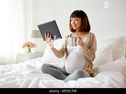 Happy pregnant asian woman with tablet pc at home Banque D'Images