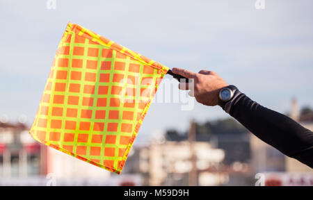 Assistant arbitre football soccer observe le match et soulève le drapeau avec sa main. Ciel bleu et bâtiments brouillée, l'arrière-plan vue en gros plan. Banque D'Images