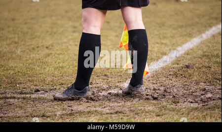 Arbitre football soccer assistant se place à côté de coin avec des chaussures pleine de boue et d'un drapeau à la main. Blur green field background, Close up. Banque D'Images