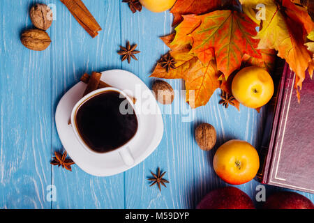 Le café dans une tasse et soucoupe blanc parmi des pommes mûres de noix, cannelle et anis. Les feuilles tombées d'érable avec un livre sur un tableau bleu. Vue d'en haut Banque D'Images