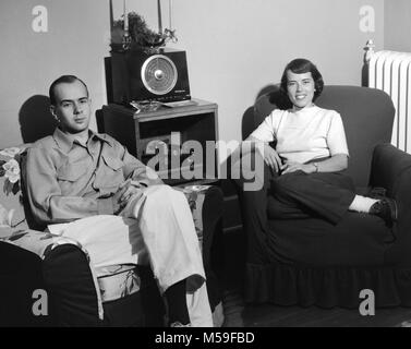 Jeune couple profitez du temps dans leur salon avec leur radio et système de son de la platine, ca. 1950. Banque D'Images