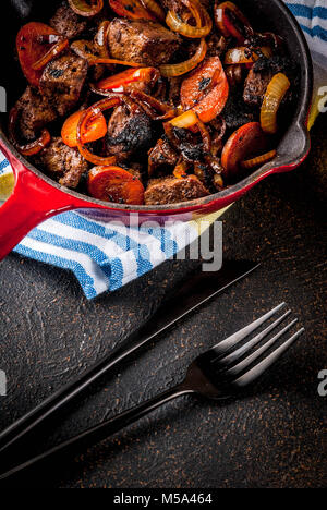 Foie de boeuf grillé ou rôti avec l'oignon et la carotte dans une poêle portionné, sombre tableau rouillé copy space Banque D'Images