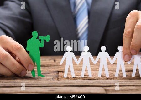 Portrait of businessman holding green paperman parlant à travers un mégaphone avec team on wooden table Banque D'Images