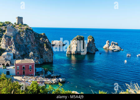 Scopello, Italie - 7 août 2017 : les falaises sur la côte avec la tonnara et les tourelles d'un château médiéval en été avec des gens sur la plage en Scop Banque D'Images