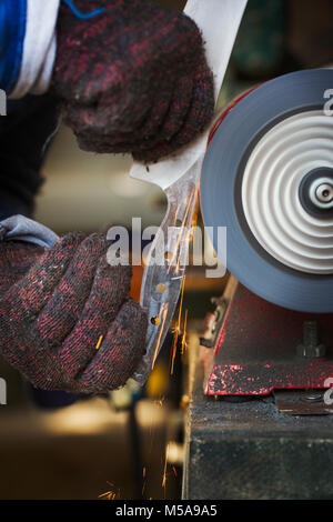 Close up of man in workshop tenant une lame fraîchement coupées, lisser la surface avec une rectifieuse plane en rotation. Banque D'Images