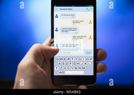 Close-up of a l'envoi de message texte à partir de téléphone mobile sur fond bleu Banque D'Images