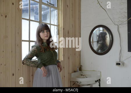 Portrait d'une belle jeune fille avec de longs cheveux noirs et les yeux bruns portant une veste verte- elle est près d'un lavabo et se reflète dans un miroir Banque D'Images