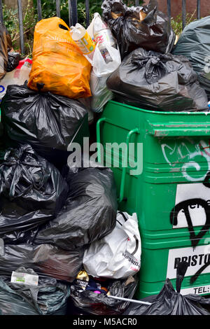 Déchets et ordures ménagères dans des sacs poubelle noirs empilés à côté de poubelle débordants, UK Banque D'Images