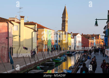 Le clocher de l'église San Martino au coucher du soleil, l'île de Burano, Venise, Vénétie, Italie avec des réflexions sur le canal et les gens qui marchent sur la Fondamenta PSE Banque D'Images