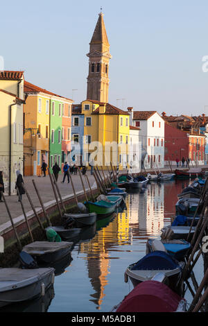 Coucher du soleil sur l'île de Burano, Venise, Vénétie, Italie avec le clocher de l'église San Martino reflétée dans le canal et les uns flânant sur Fondamenta del Banque D'Images