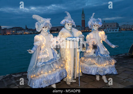 Costumes de Carnaval de Venise la nuit, Venise, Vénétie, Italie. Trois personnes en costumes classiques imcorporating feux rougeoyants posant au lagoon à blue Banque D'Images