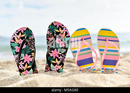 Libre de deux paires différentes de colorful flip-flops, l'un d'entre eux à motifs de fleurs et l'autre rayé, bloqué sur le sable d'une plage tranquille, avec si Banque D'Images