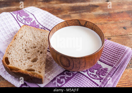 Close-up en bois une tasse de lait et une tranche de pain sont sur cuisine lilas serviettes sur la vieille table en bois. Banque D'Images