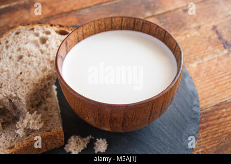 Close-up de tasse de lait et les tranches de pain sur le bord de l'ardoise ronde cuisine sur planches en bois ancienne diagonale arrière-plan. Banque D'Images