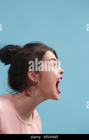 La jeune femme criant en colère émotionnelle sur fond bleu studio Banque D'Images