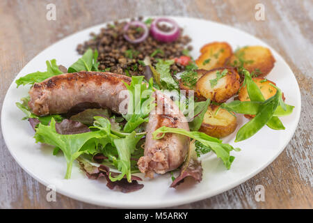 France La saucisse de Toulouse grillée avec potatoaes rôti et salade et lentilles sur le vieux fond de bois Banque D'Images