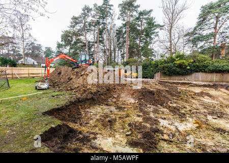 Grosse orange plante lourde mechanical digger garé sur un monticule de terre après avoir creusé les fouilles pour les fondations d'un nouveau développement résidentiel Banque D'Images