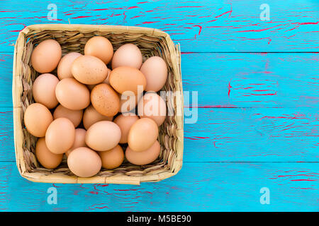 Accueil récoltés panier en osier de nutritifs frais free range oeufs brun rustique dans un panier tissé sur un fond de bois peinture crackle bleu avec l'exemplaire sp Banque D'Images