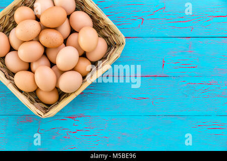 Panier en osier rustique rempli d'une saine farm fresh free range oeufs brun vue depuis le dessus sur un fond de bois peinture craquelé bleu avec copie savs Banque D'Images