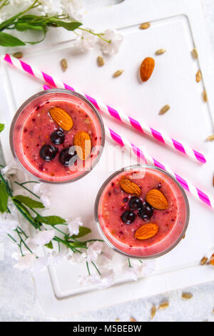 Des smoothies de fruits des bleuets, bananes et amandes dans des verres à cocktail avec tubes sur une planche de bois blanc Banque D'Images